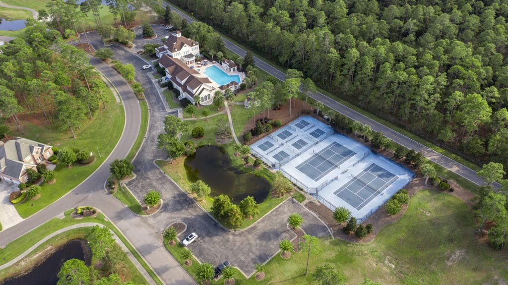 Aerial view of Rivers Edge community with tennis courts, clubhouse, pool, and lush green landscape.