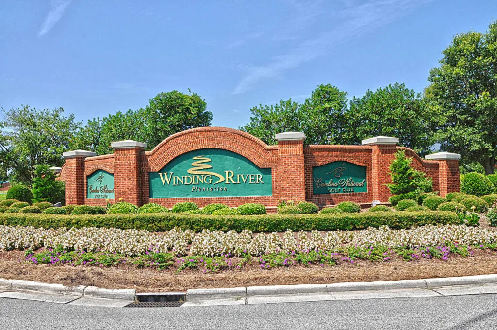 Entrance sign for Wyndsor at the River community with brick wall, greenery, and landscaped flowers.