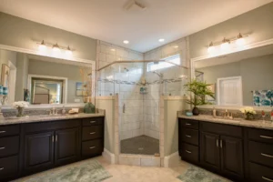 Elegant modern bathroom with glass shower, dual vanities, granite countertops, and warm ambient lighting.