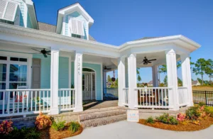 Light blue coastal home with white porch, dormer windows, and charming seaside landscaping.