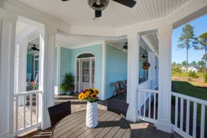 Coastal blue house porch with sunflowers, white trim, and wooden seating for relaxing outdoors.