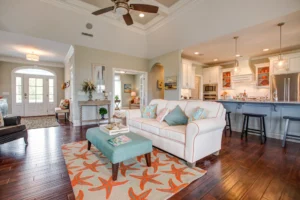 Coastal open-concept living room with cream sofa, turquoise ottoman, and bright beach-inspired décor.