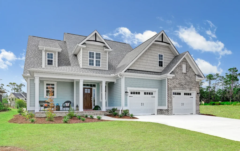Modern blue farmhouse with white trim, front porch, two-car garage, and landscaped green lawn.