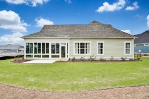 Modern suburban home with sunroom, gray roof, and spacious green backyard under blue sky.