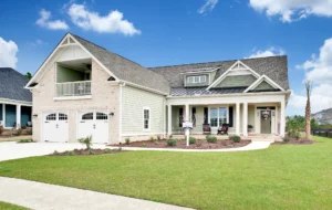 Modern farmhouse with front porch, two-car garage, light siding, and landscaped lawn under blue sky.