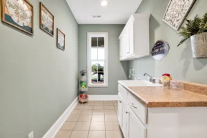 Olive green laundry room with white cabinets, tan countertops, natural light, and modern decor.
