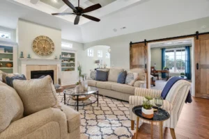 Warm farmhouse living room with beige sofa, fireplace, rustic clock, and wooden barn doors.