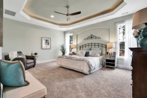 Elegant master bedroom with tray ceiling, neutral colors, cozy seating, and soft natural lighting.