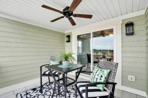 Cozy sage-green balcony with black metal seating, potted plant, ceiling fan, and tropical decor.