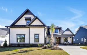 Modern white farmhouse with black trim, gabled roof, wood accents, and sunny landscaped yard.