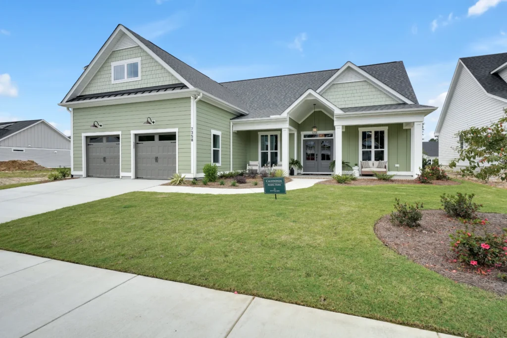 Modern sage green single-story home with white trim, two-car garage, and manicured front lawn.