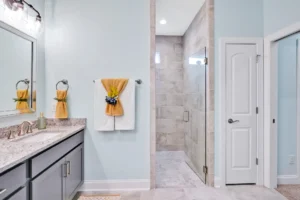 Modern light blue bathroom with granite vanity, decorative towels, and a glass walk-in shower.