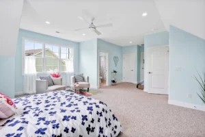 Bright blue bedroom with natural light, floral bedding, and cozy sitting area.