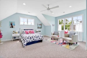 Bright pastel blue bedroom with cozy bed, pink accents, and natural light-filled sitting area.