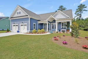Charming modern blue cottage with white trim, front porch, two-car garage, and lush green lawn.
