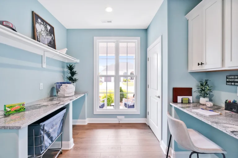 Bright coastal blue flex room with window workspace, white cabinets, and warm wood flooring.