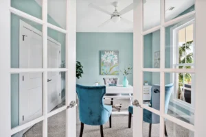 Bright coastal home office with turquoise walls, white desk, and natural light through French doors.