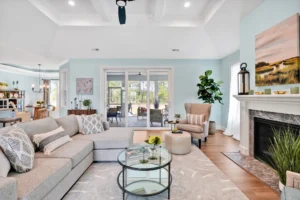 Modern living room with sectional sofa, glass tables, white fireplace, and natural light.