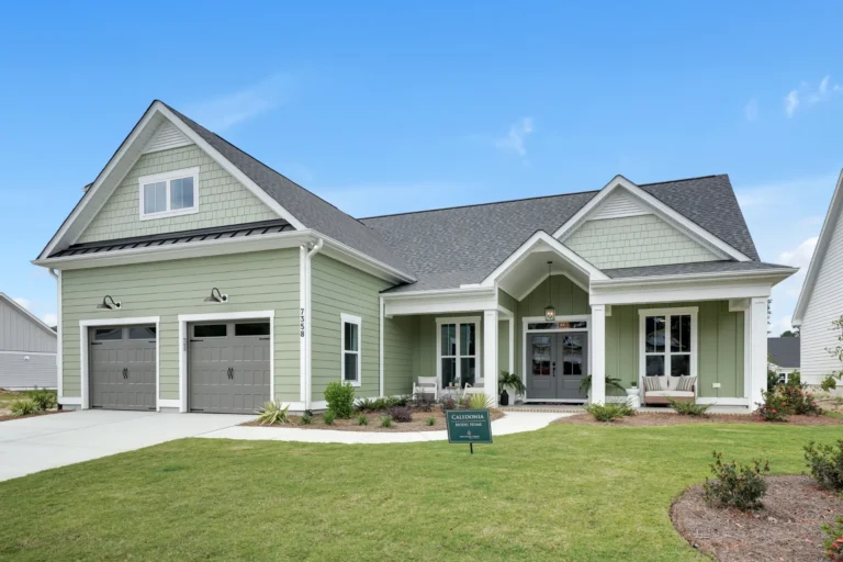 Modern green single-story home with white trim, gabled roof, and landscaped yard in Brunswick Forest.