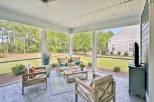 Modern screened patio with wooden furniture, colorful cushions, and serene backyard views.