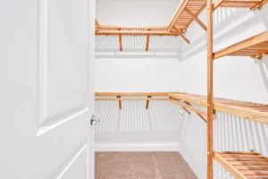 Spacious modern walk-in closet with white walls, wooden shelves, and soft tan carpet flooring.