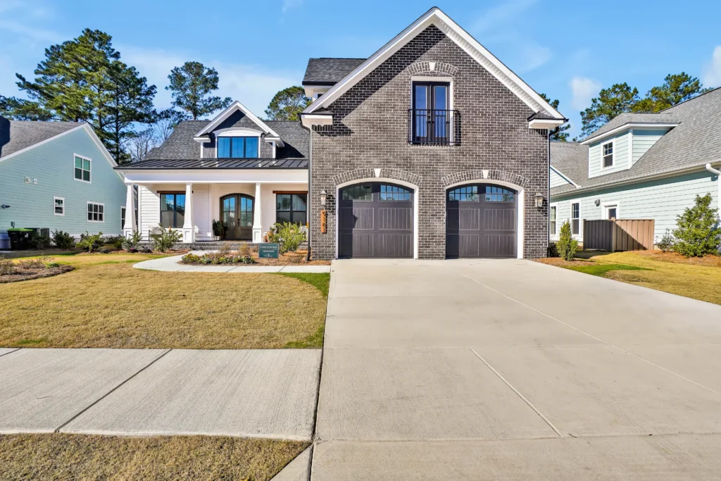 Modern suburban home with dark brick exterior, wooden garage doors, and inviting covered porch.