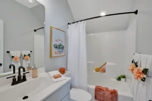 Modern white bathroom with black fixtures, coral accents, and cozy minimalist design.