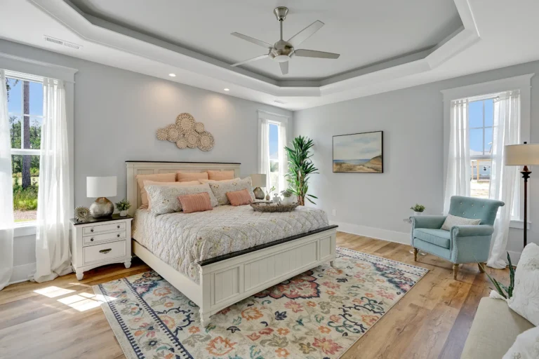 Bright coastal farmhouse bedroom with white bed, pastel decor, wood floors, and natural light.