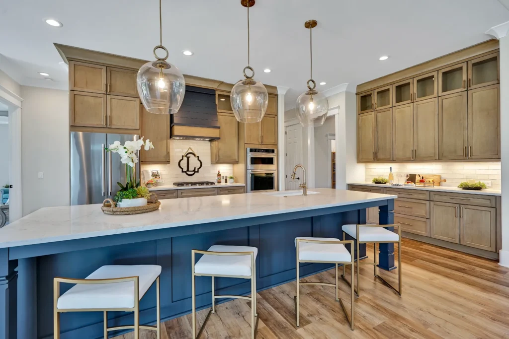 Modern kitchen with navy island, white marble countertop, gold stools, and tan cabinetry.