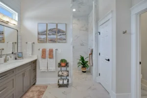 Bright modern marble bathroom with double vanity, glass shower, terracotta accents, and greenery.