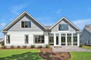 Modern white farmhouse with large windows, dark roof, and tidy lawn under a blue sky.