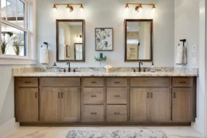 Modern double vanity bathroom with light wood cabinets, granite countertop, and warm industrial lighting