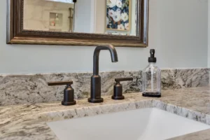 Modern bathroom sink with granite countertop, white undermount basin, and matte black faucet fixtures.