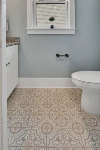 Modern bathroom with gray-blue walls, patterned tile floor, white vanity, and natural light.