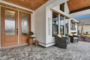 Modern farmhouse porch with wooden double doors, wicker chairs, and stone flooring.
