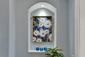 Arched alcove with illuminated floral painting, blue glass accents, and green plant décor.