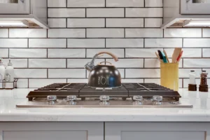 Modern white kitchen with stainless steel gas cooktop, black kettle, and yellow utensil holder.