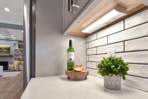 Modern white kitchen countertop with wine, wooden tray, and potted plant under warm lighting.