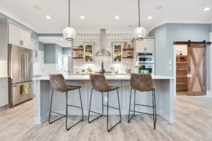 Bright modern farmhouse kitchen with quartz island, leather stools, wood accents, and stainless appliances.