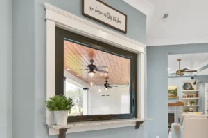 Modern farmhouse interior with black-framed pass-through window, blue-gray walls, and wood-accented patio.
