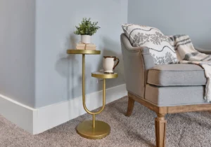 Modern cozy reading nook with gray armchair, gold side table, books, and potted plant.