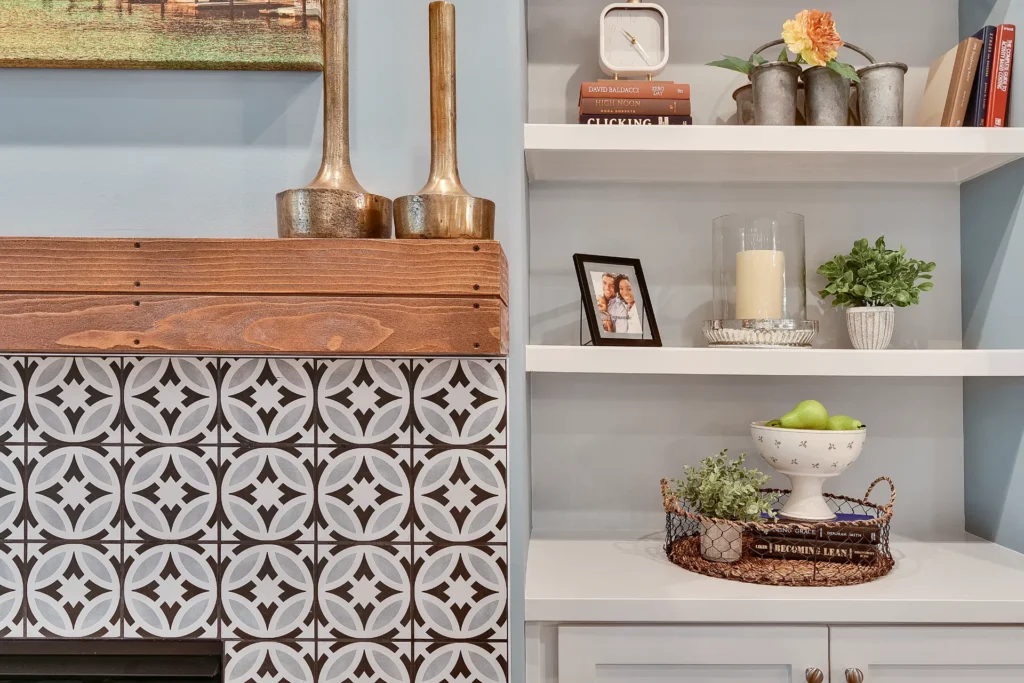 Farmhouse living room with tiled fireplace, wooden mantle, and white shelves decorated with cozy accents.