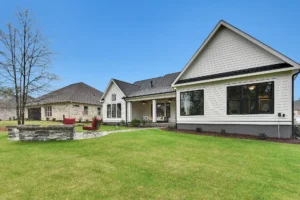 Modern suburban home with white siding, red fire pit chairs, and a green landscaped lawn.