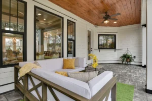Modern outdoor patio with wooden ceiling, glass windows, and cozy L-shaped seating area.