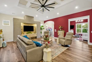 Modern living room with red accent wall, beige leather seating, stone TV wall, and hardwood floors.