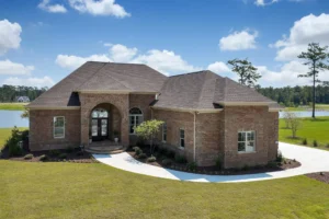 Elegant single-story brick lakefront home with lush green lawn and scenic waterfront view.