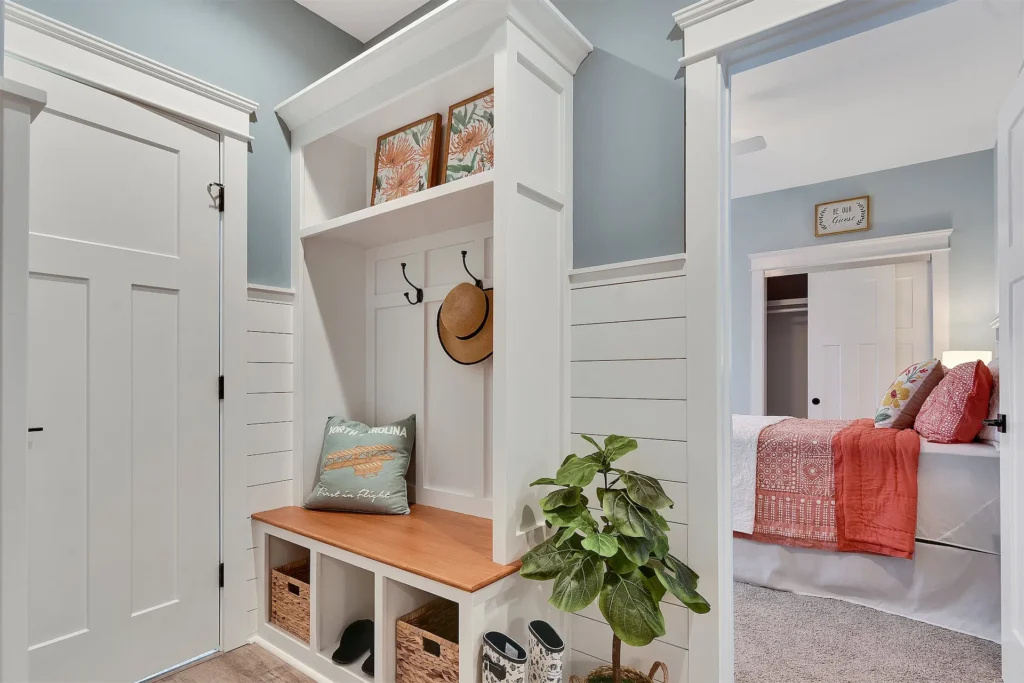 Cozy blue-gray entryway with white bench, woven baskets, and view into coral-accented bedroom.