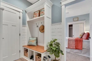 Cozy blue-gray entryway with white bench, woven baskets, and view into coral-accented bedroom.