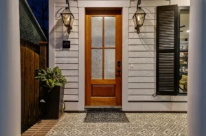 Warm wooden front door with frosted glass, patterned tile porch, and black lantern lights.