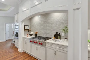 Modern kitchen with arched range, stainless-steel stove, gray cabinets, marble countertop, and hardwood floors.